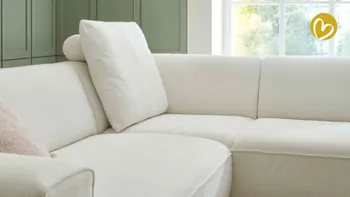 Detailaufnahme einer hellen Sofaecke mit abnehmbarem Rückenkissen und Kopfstütze, umgeben von grün getäfelter Wand und großem Fenster mit natürlichem Lichtern